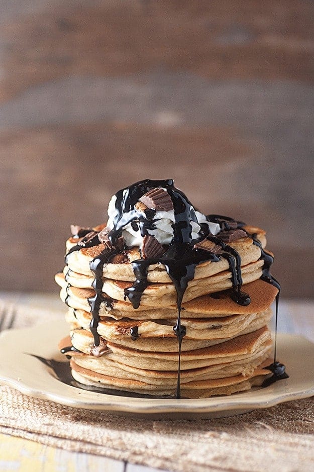 Several stacked pancakes topped with pieces of peanut butter cups and chocolate syrup.