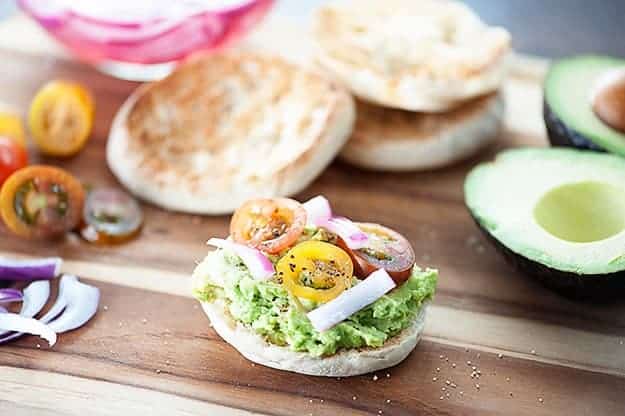 These English muffins are topped with smashed avocados, pickled onions, and cherry tomatoes for a quick breakfast or snack recipe that is filling and satisfying!