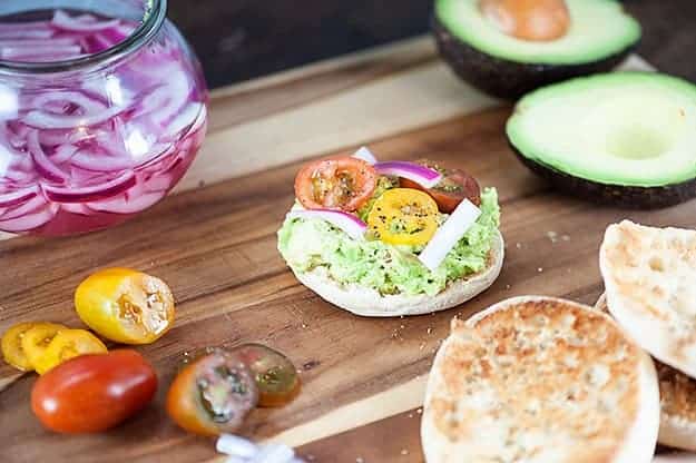 These English muffins are topped with smashed avocados, pickled onions, and cherry tomatoes for a quick breakfast or snack recipe that is filling and satisfying!