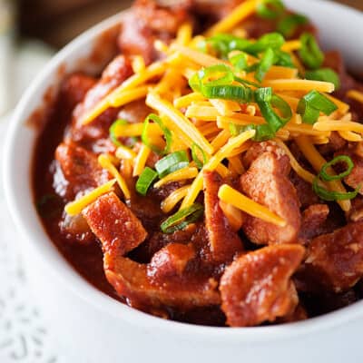 A close up of a cup of chili topped with shredded cheese.