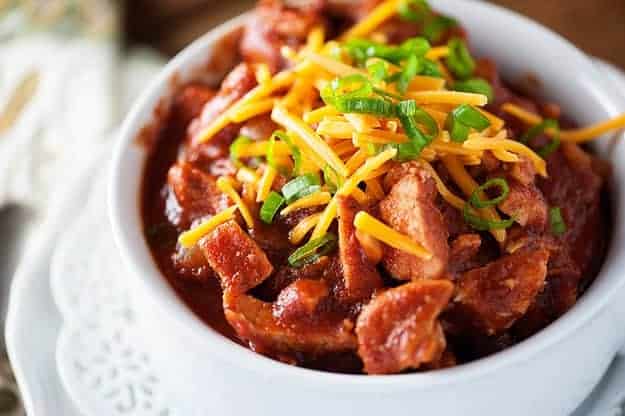 A close up of a cup of chili topped with shredded cheese.