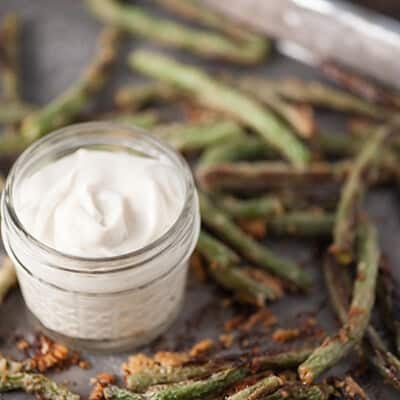 A jar of sauce on a baking sheet with a bunch of green beans.