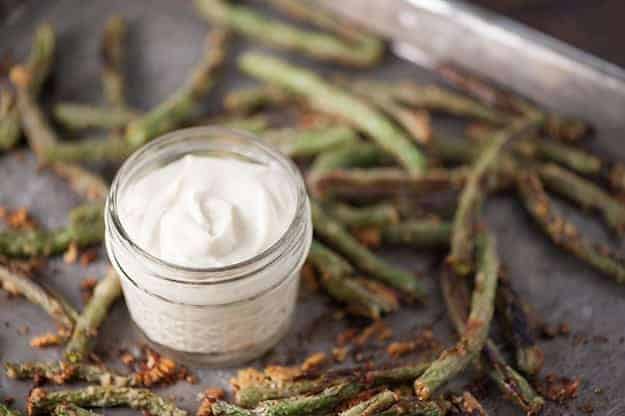 A jar of sauce on a baking sheet with a bunch of green beans.