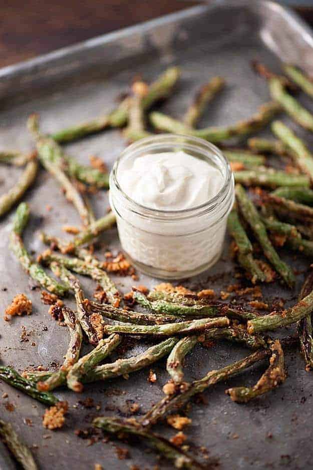 Parmesan coated green beans on a baking sheet with a jar of white dipping sauce.