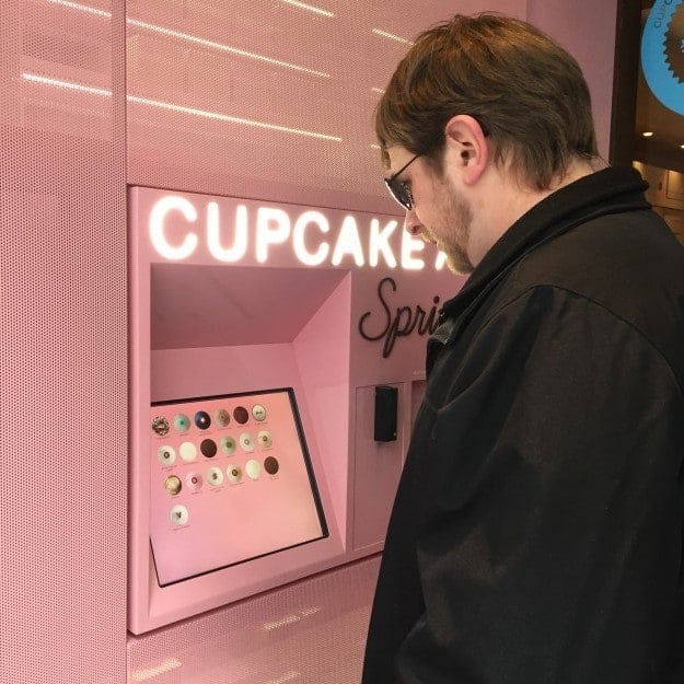 A man standing in front of a cupcake ATM.