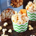 Paper cups of cheesy popcorn on a wooden table in front of a popcorn cookbook.