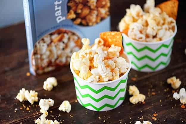Paper cups of cheesy popcorn on a wooden table in front of a popcorn cookbook.