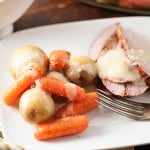 Potatoes and carrots to the side of sliced pork on an oval white plate.