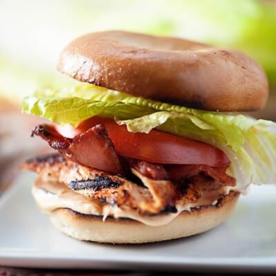 A spicy chicken sandwich with tomatoes and lettuce on a square plate.