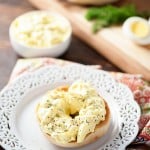 Egg salad on a bagel on a decorative white plate.