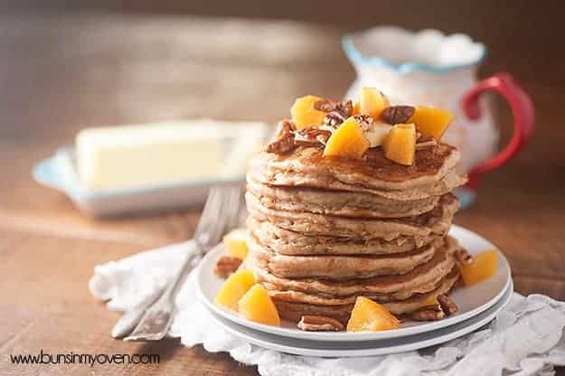 A large stack of pancakes topped with peaches and pecans.