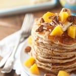 A stack of pancakes topped with peach chunks and pecans.