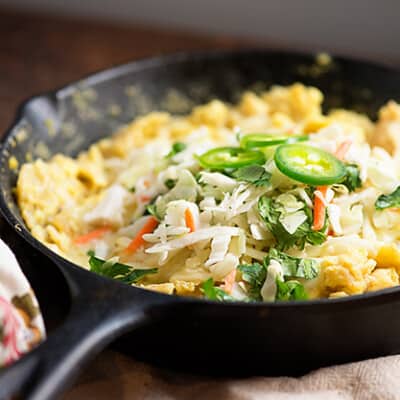 A cast-iron skillet on a dishtowel with jalapenos, eggs, and cheese.