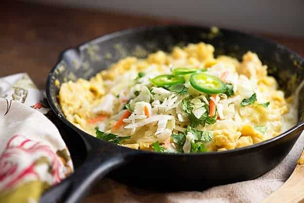 A cast-iron skillet on a dishtowel with jalapenos, eggs, and cheese.