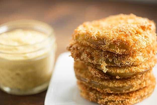 Fried green tomatoes on a square plate next to a jar of remoulade.