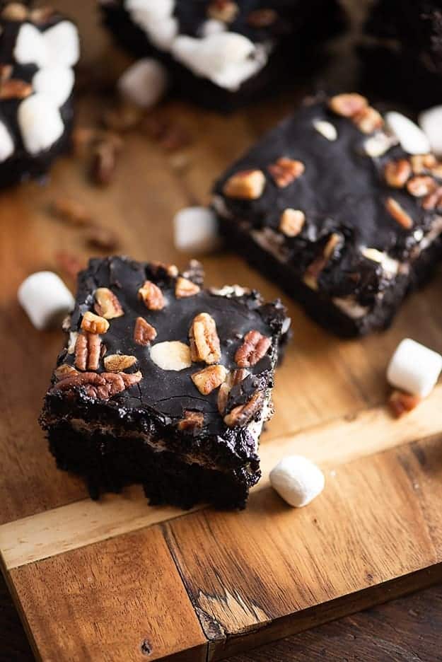 A couple chocolate brownies on a cutting board with mini marshmallows on a cutting board.