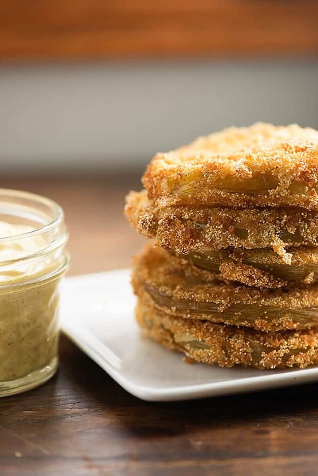 A small jar of cajun remoulade next to a stack of fried green tomatoes.