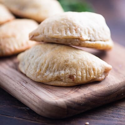 A close up of a couple of empanadas stacked on a narrow wooden cutting board.