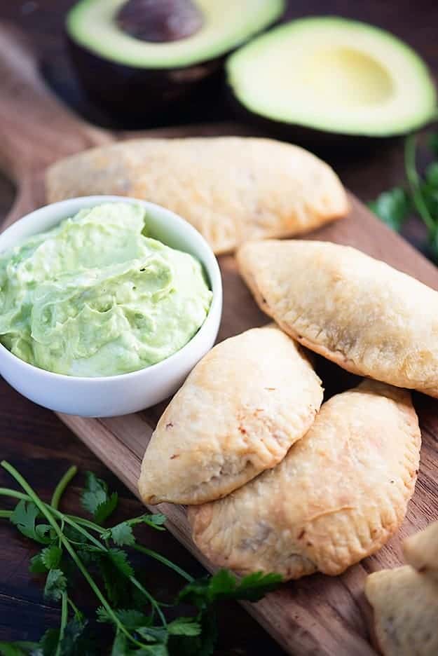 A close up of carnitas empanadas next to a white bowl of dip.