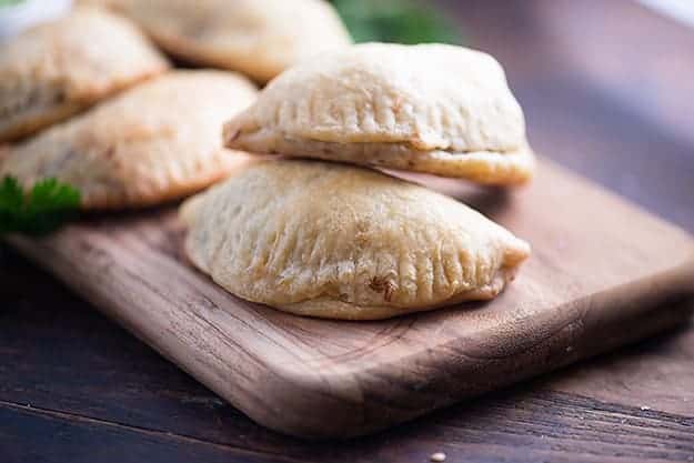 A close up of a couple of empanadas stacked on a narrow wooden cutting board.