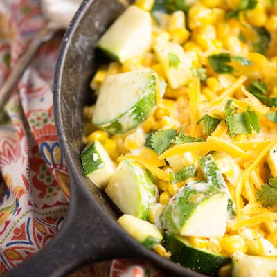 Close up of a cast-iron skillet with shredded cheese, corn, and zucchini.