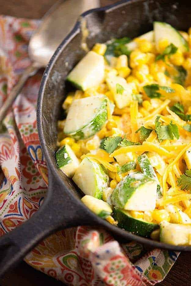 Close up of a cast-iron skillet with shredded cheese, corn, and zucchini.