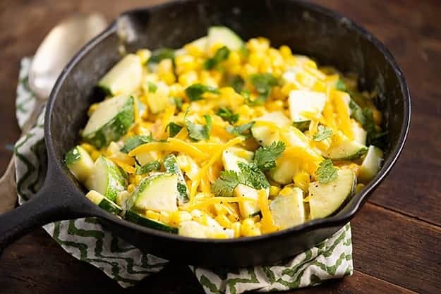 A cast-iron skillet wtih zucchini chunks, shredded cheese, and corn in it.