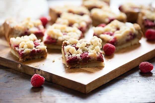 Raspberry crumb bars and loose raspberries on a wooden cutting board.