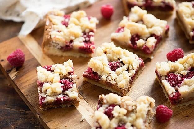 A close up of several raspberry crumb bars on a cutting board.