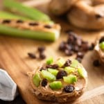 A wooded cutting board with raisins and bagels on it.