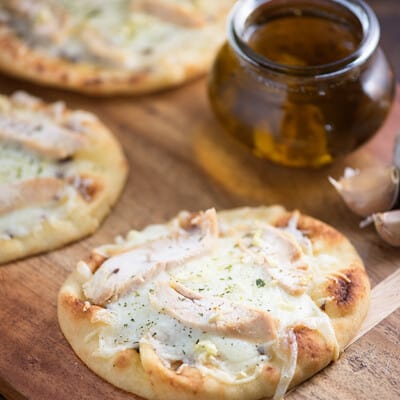 Several chicken flatbreads on a cutting board with a jar of garlic oil.