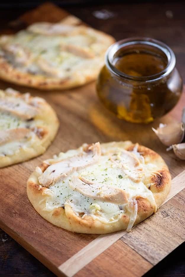 Several chicken flatbreads on a cutting board with a jar of garlic oil.