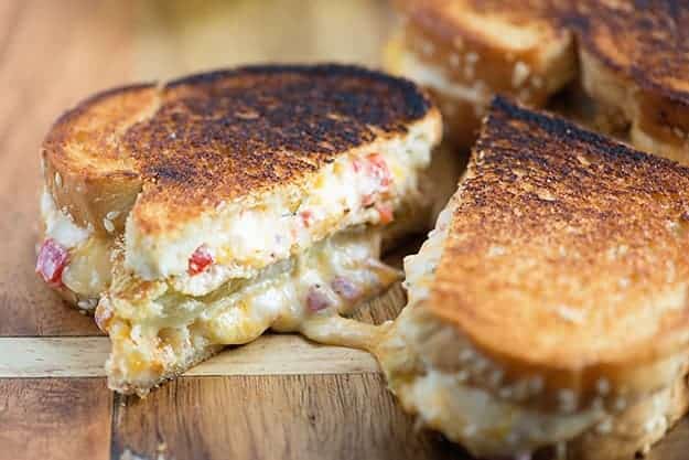 A grilled cheese sandwich with green tomatoes cut in half on a cutting board.