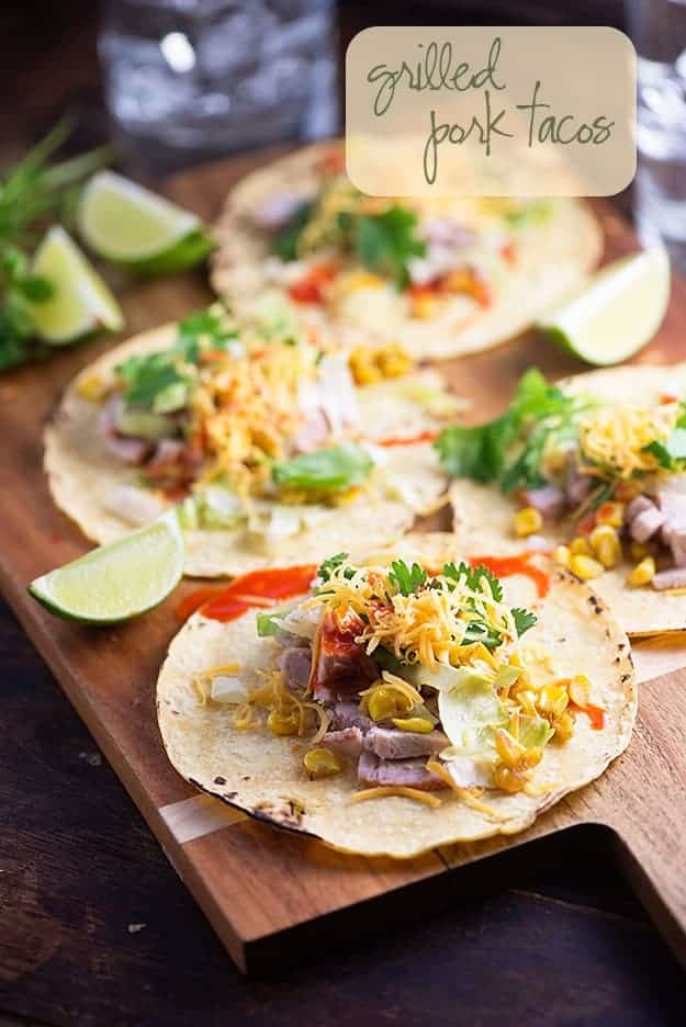 Open face tacos on a wooden cutting board with lime wedges.