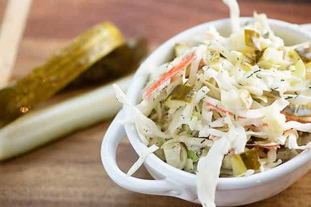 Close up of a bowl of cole slaw on a wooden cutting board in front of pickle spears.