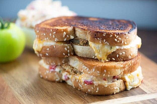 Two grilled cheese and tomato sandwiches stacked on a cutting board.