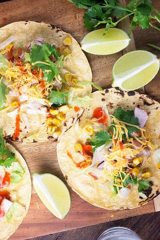 An overhead view of pork tacos on a table surrounded by lemon wedges.