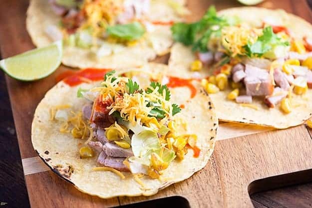 Open face pork tacos on a wooden cutting board.