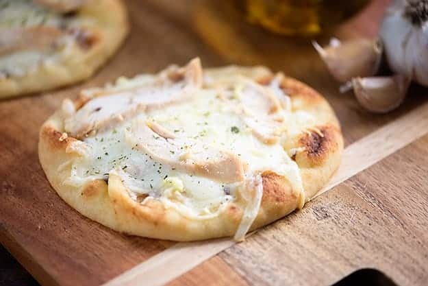 Chicken topped flatbread on a cutting board.