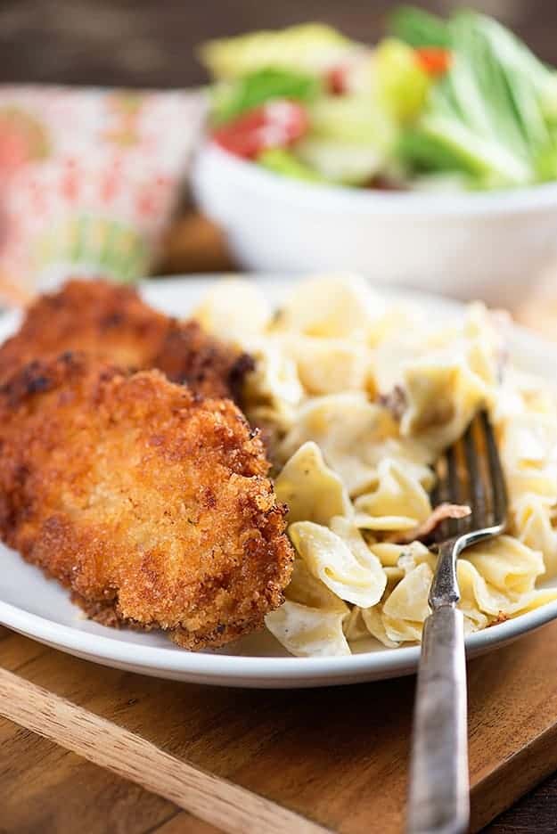A couple of breaded pork chops on a plate with noodles.