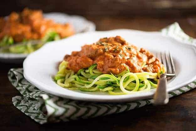 Zucchini noodle spaghetti on a small white plate sitting on top of a cloth napkin.