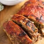 A loaf of meatloaf on a cutting board partially sliced.