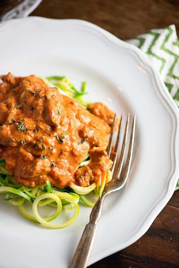 Topdown view of a plate of zucchini noodles on a decorative white plate with a fork on it.