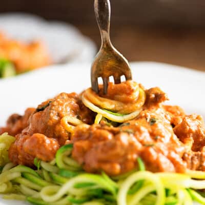 A fork stabbing downward into a plate of spaghetti and spinning the spaghetti noodles.