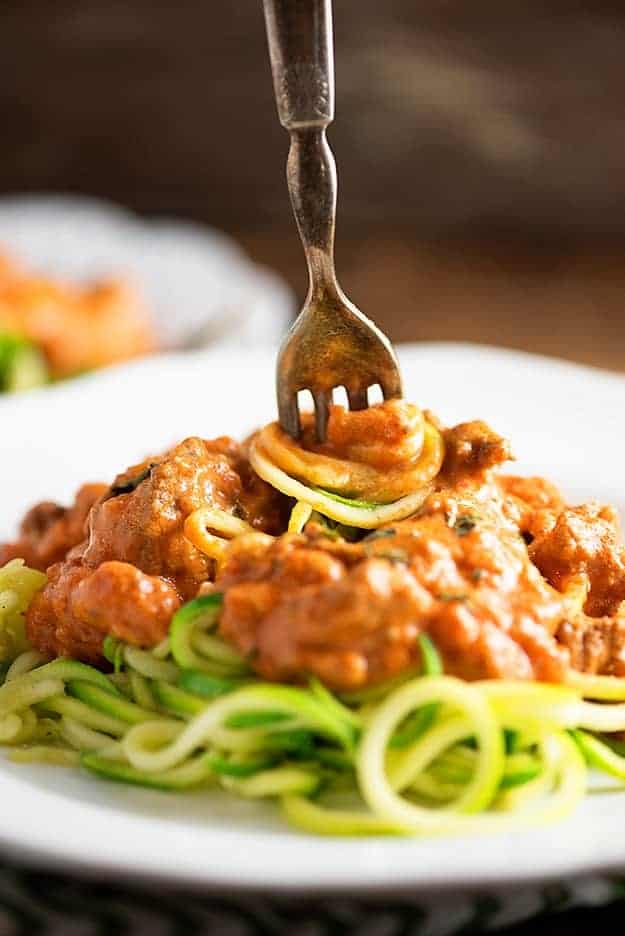 A fork stabbing downward into a plate of spaghetti and spinning the spaghetti noodles.