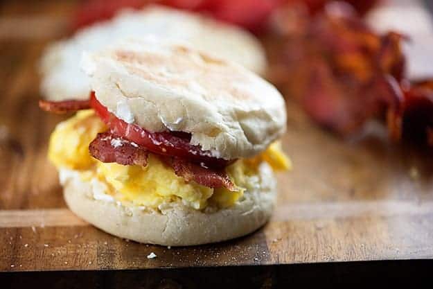 A breakfast biscuit with tomato on a wooden cutting board 