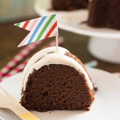 A close up of a piece of chocolate cake on a plate with a tiny colorful flag in it.