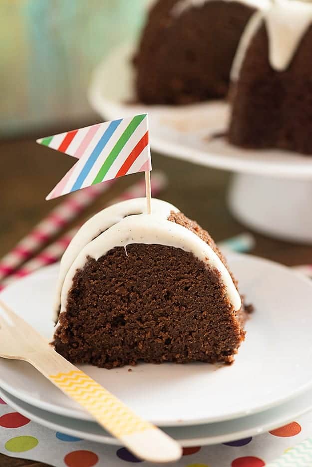 A close up of a piece of chocolate cake on a plate with a tiny colorful flag in it.