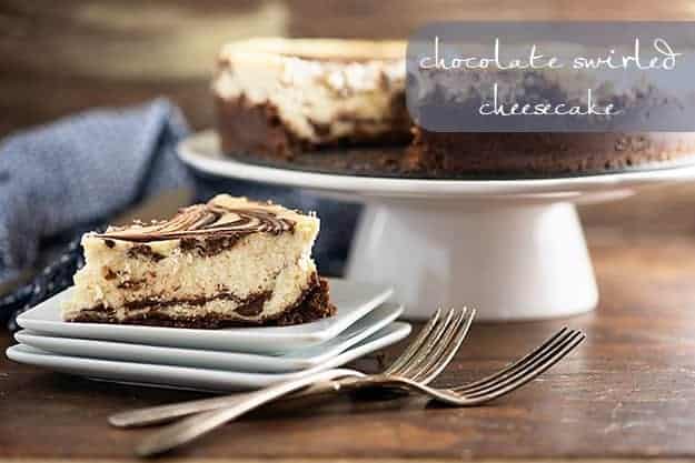 A piece of chocolate swirl cheesecake on a square plate in front of a cheesecake on a cake stand.