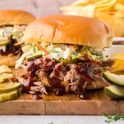 A close up of a pulled pork and coleslaw sandwich on a wooden cutting board.